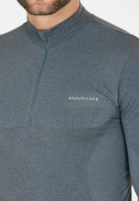 Grå langærmet atletisk top med lynlås krave, tekstureret stof på brystet og glat nederste sektion. Har "ENDURANCE" logo i hvid.
