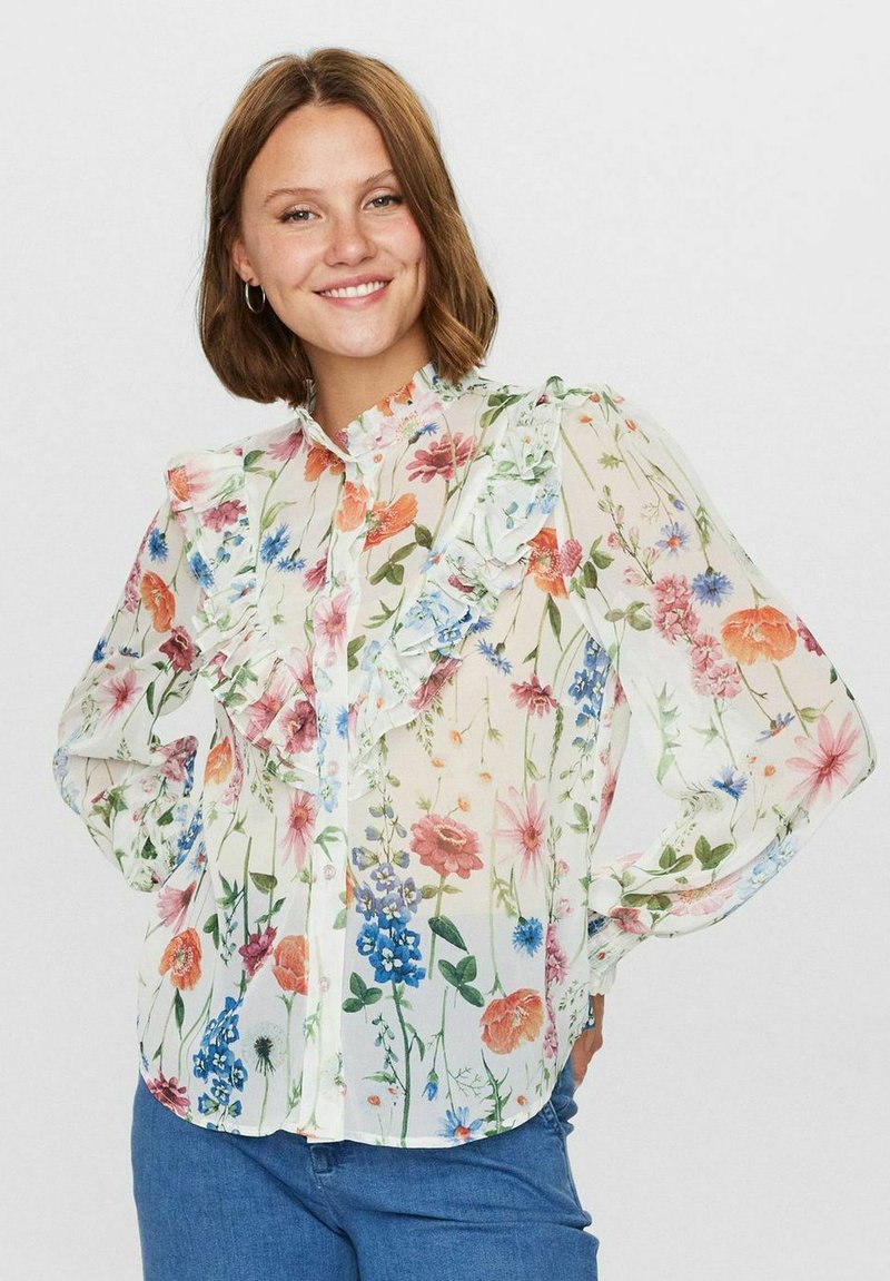 Genomskinlig blus med blommönster och volangkrage samt långa ärmar, som har flerfärgade blommor på en ljus bakgrund. Knäppning framtill.