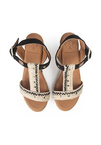 Sandalias de tiras beiges tejidas con tela negra y hebilla ajustable en el tobillo, con costuras decorativas y detalles en tono dorado.