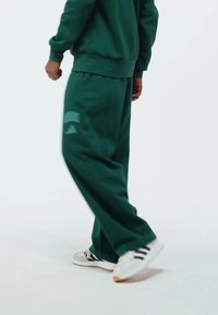 Gröna sweatpants i mjukt tyg, med elastisk midja och avslappnad passform. Bärs med vita sneakers och svarta ränder.