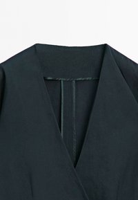 Close-up of black garment with a deep V-neckline and visible inner seam tape along the collar and back opening.