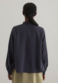 Marineblaue, langärmelige Bluse aus weichem Material mit Kragen, in lässigem Schnitt und mit gerafften Manschetten, getragen über einem hellen Rock.