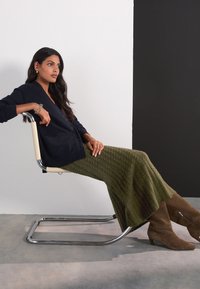 Navy cardigan with button front, ribbed texture, and patch pockets; olive-green, textured maxi skirt; brown knee-high boots with block heel.