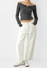 Grey ribbed off-the-shoulder sweater with a zip closure, paired with loose-fitting white pants featuring contrasting stitching and wide leg design.