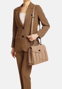 Borsa beige con un design strutturato, caratterizzata da pieghe e una chiusura a pattina. Completata da una tracolla regolabile e dettagli metallici.