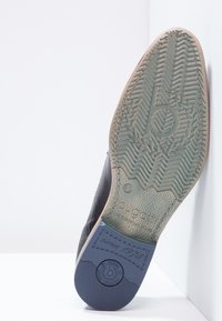 Semelle de chaussure en caoutchouc bleu foncé avec un design texturé ; logo en relief et détail "depuis 1978" sur une section beige plus claire.