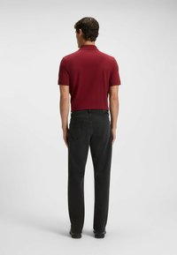 Polo shirt bordeaux a maniche corte, abbinato a jeans neri. L'outfit mostra una trama di tessuto liscia e un design aderente sul retro.