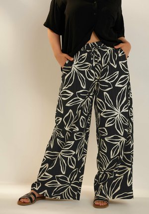 Pantalones de pierna ancha en tela negra con patrones de hojas blancas. Cintura elástica, bolsillos laterales y acabado texturizado. Combinados con sandalias planas.