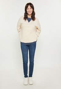 Felpa crema con scollatura a V, dettagli blu navy e vestibilità rilassata, abbinata a jeans skinny blu scuro e sneaker bianche.