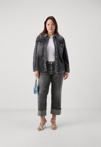 Denim jakna in jeans v zbledeli črni barvi, s podrobnostmi na gumbih in zavihanimi manšetami. Bele majice pod njimi, srebrne sandale in svetlo modra torbica.