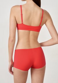 Un reggiseno sportivo rosso e mutandine coordinate, design senza cuciture, spalline regolabili, texture liscia e stile minimalista sulla schiena di un modello.