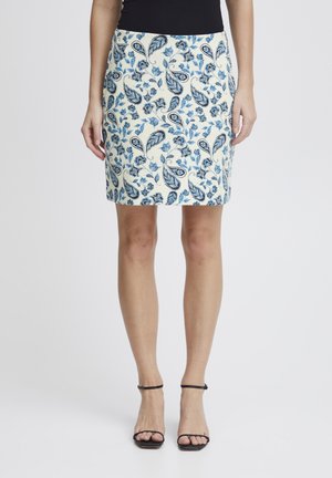 Jupe blanche avec un motif floral paisley bleu, design ajusté, ourlet uni, associée à des sandales à lanières noires. Texture lisse, longueur genou.