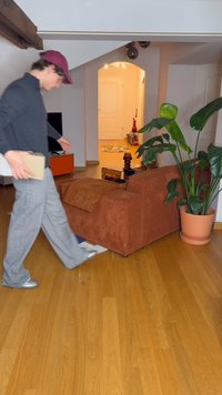 Brown corduroy armchair with a textured cushion, surrounded by a potted plant, hardwood floor, and a softly lit doorway in the background.