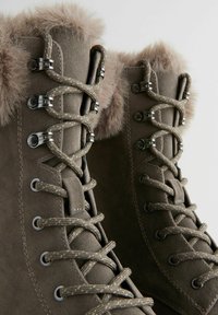 Braune Wildleder-Schnürstiefel verfügen über einen Kunstfellkragen, Metallösen und strukturierte Schnürsenkel, die ein strapazierfähiges Design für kaltes Wetter hervorheben.