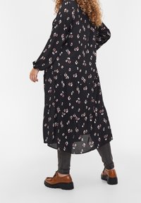 Svart klänning med blommönster, långa ärmar, lagerdesign och en lös passform, kombinerad med mörka jeans och bruna snörboots.