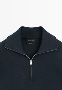 Bavlněný pulovr v tmavě námořnické modři s límečkem na půl zip, žebrovanou texturou a stříbrným zipem. Štítek nese nápis "Massimo Dutti".