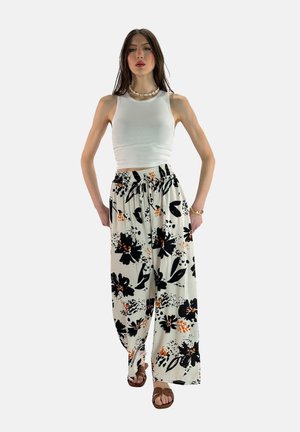 Hvid tanktop og bukser med elastisk talje, der har et blomstermønster i sort og orange på en lys baggrund, parret med brune sandaler.