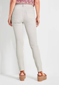 Hellgraue Skinny-Jeans mit detaillierten Gesäßtaschen und Gürtelschlaufen, kombiniert mit braunen Plateausandalen. Glatter Stoff mit leichtem Stretch.