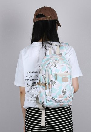 Light blue and cream backpack with floral patterns, multiple zippered pockets, and beige accents. Adjustable straps and top handle for convenience.