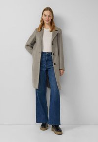 Jasnoszary płaszcz z mieszanki wełny z klapowym kołnierzem i zapięciem na guziki, noszony na białej bluzce i wysokich, rozkloszowanych jeansach w kolorze niebieskim.