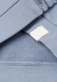 Světlá modrá tkanina se zipem a bílou štítkem s embosovaným logem králíka na měkkém pleteném materiálu.