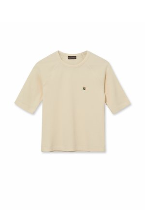 Bež kratka majica z teksturo, zaokroženim izrezom in majhnim vezenim cvetličnim detajlom na levi strani prsnega koša.