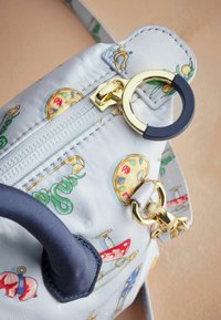 Ljusblå handväska med olika färgade konstnärliga mönster. Har en guldfärgad dragkedja, marinblå detaljer och en dekorativ guldringsfäste.