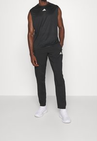 Svart ärmlös träningströja med vitt logotyp, kombinerad med svarta träningsbyxor med vit logotyp och vita sneakers.