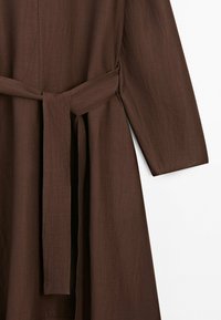 Manteau en tissu marron texturé avec manches longues et une large ceinture à nouer à la taille.