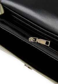 Interior de un bolso de mano de cuero sintético negro, con un bolsillo con cremallera, textura suave y una cremallera metálica con una pestaña de tirón plateada.