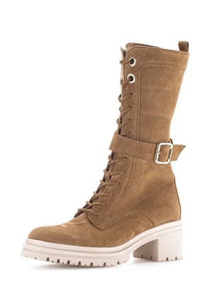 Beiger Wildleder-Stiefel bis zur Mitte der Wade mit Schnürung, weißer, klobiger Sohle und dekorativem Schnallenriemen an der Seite.