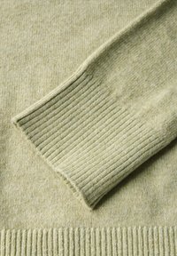 Ljusgrön tröja med en mjuk, texturerad yta. Har ribbade mudd och nederkant, vilket indikerar en stickad design.