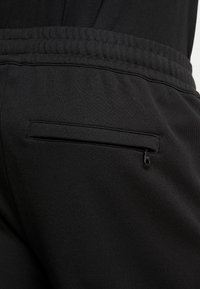 Pantalones de chándal negros con un material suave, cinturilla elástica y un pequeño bolsillo con cremallera en la parte posterior para un almacenamiento seguro.