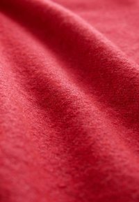 Red woolen fabric with a soft texture, displaying subtle variations in shading and light. Surface appears slightly fuzzy and smooth.