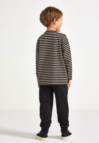 Gestreifte Langarmbluse in Schwarz und Beige, kombiniert mit schwarzen Jogginghosen. Die Bluse hat horizontale Streifen und einen lockeren Schnitt.
