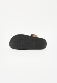 Brune semskede sandaler med en teksturert svart gummisåle. Sålen har trykte merkeinntrykk og størrelseinformasjon.