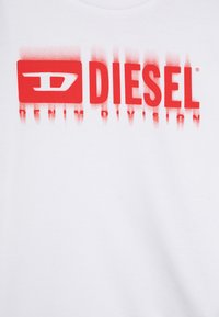 T-shirt bianca in cotone con un grande logo rosso grafico con la scritta "DIESEL" e "DENIM DIVISION" con effetto spray.