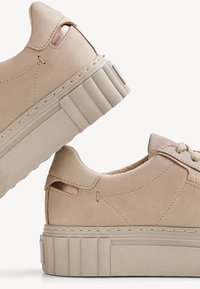Beige leather sneakers with a textured platform sole, featuring side cutouts and contrasting accents. Stitched detailing along the upper.