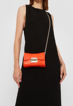 Woman in sleeveless black dress wearing a small bright orange leather crossbody bag with gold clasp and chain strap.