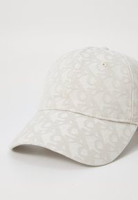 Baseball cap in light beige fabric with a subtle tonal pattern. Features a curved brim and stitched detailing along the crown.