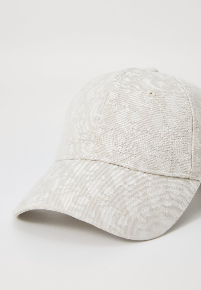 Gorra de béisbol en tela beige claro con un sutil patrón tonal. Presenta una visera curva y detalles cosidos a lo largo de la corona.