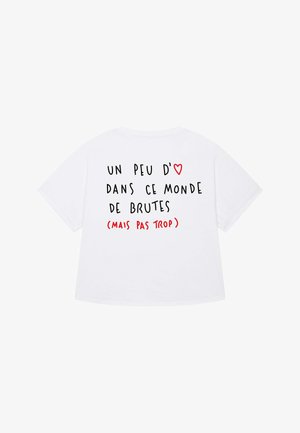 Balta kokvilnas T-kreklā ar īsām piedurknēm, uz muguras redzams melns un sarkans teksts, kas izsaka vēstījumu franču valodā.