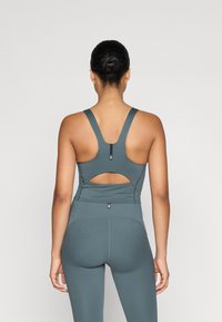 Sportiska tvertne t-krekli tumši tirkīza krāsā ar racerback dizainu, kas piedāvā izgriezumu un gludu, elastīgu audumu komfortam.