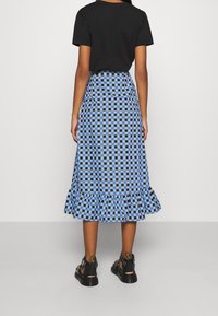 Midi-Rock mit blauem und schwarzem Karomuster und Rüschensaum, aus leichtem Material gefertigt. Kombiniert mit schwarzen Riemchensandalen.