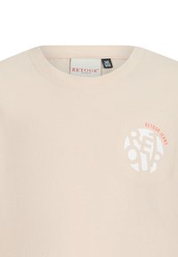 T-shirt in cotone beige chiaro con scollatura rotonda. Presenta un logo circolare con testo bianco e corallo "RET" e "JEANS" sul fronte.