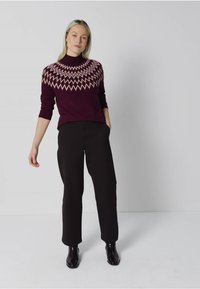 Bordeaux gestrickter Pullover mit einem cremefarbenen Zickzackmuster am Kragen, kombiniert mit schwarzen Hosen und Knöchelschuhen, was eine enganliegende Silhouette schafft.