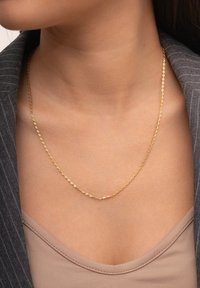 Gouden kettinghalsband met ovale schakels, dicht bij de nek hangend. Draag het over een beige top en combineer het met een grijze pinstripe blazer.