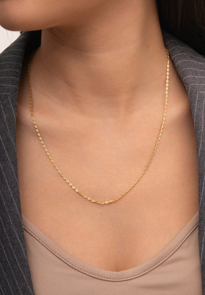 Gouden kettinghalsband met ovale schakels, dicht bij de nek hangend. Draag het over een beige top en combineer het met een grijze pinstripe blazer.