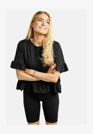 Czarny top z falbankami na rękawach i marszczonym dołem, w połączeniu z czarnymi krótkimi spodniami rowerowymi. Materiał wydaje się miękki i dopasowany do sylwetki.