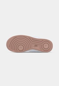 Semelle d'une sneaker Nike présentant des motifs circulaires de la semelle et le logo Nike au centre, montrée sur un fond clair uni.